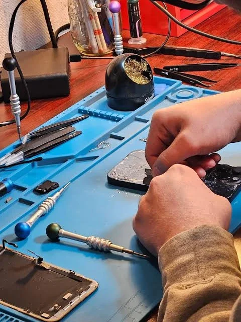 Repair bench with precision screwdrivers, tweezers and a cracked phone being opened